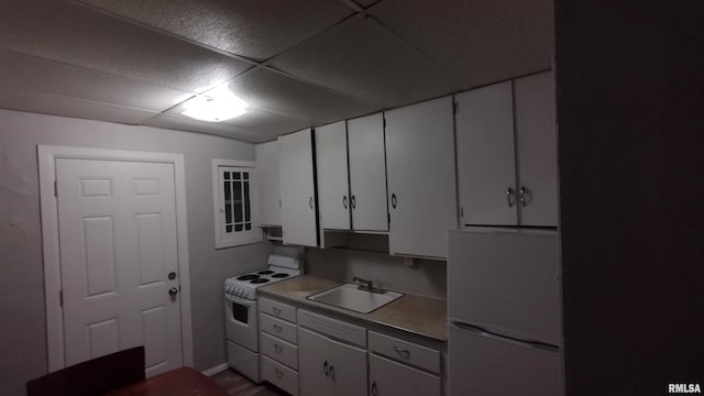 kitchen with white appliances, a drop ceiling, white cabinets, and a sink