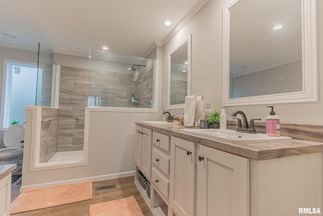 full bathroom with double vanity, a tile shower, a sink, and wood finished floors