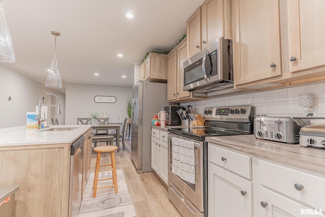 kitchen featuring appliances with stainless steel finishes, light countertops, light brown cabinetry, light wood-style floors, and a sink