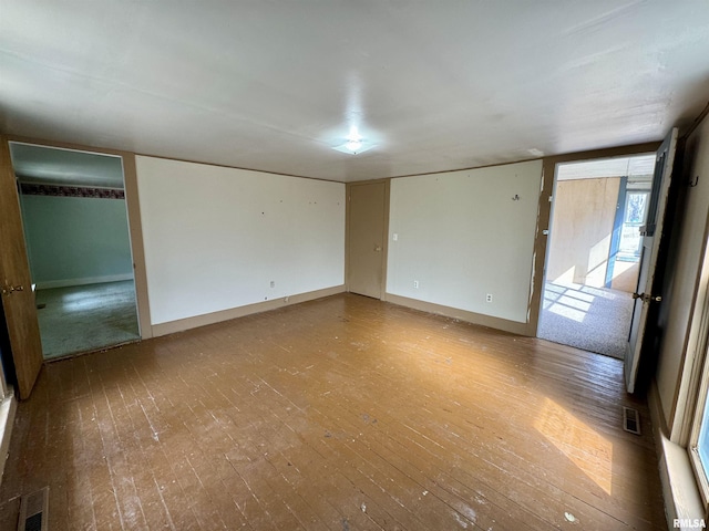 empty room featuring wood-type flooring, visible vents, and baseboards