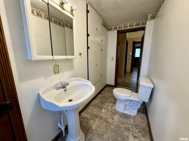 bathroom with toilet, a sink, baseboards, and a textured ceiling