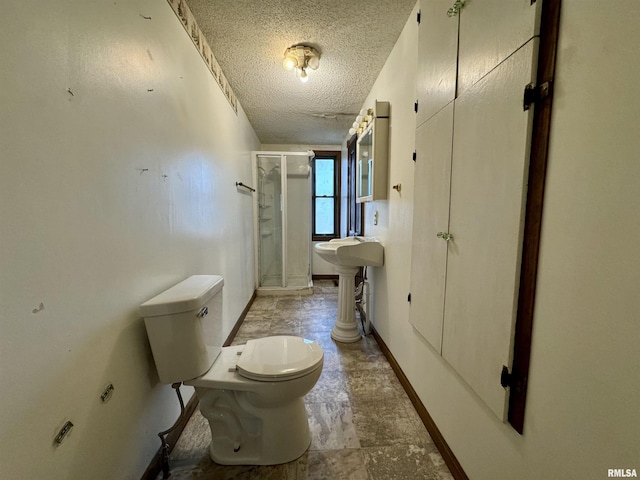 bathroom with a textured ceiling, toilet, baseboards, stone finish flooring, and a stall shower