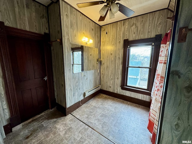 empty room featuring a baseboard heating unit, ceiling fan, wood walls, and baseboards