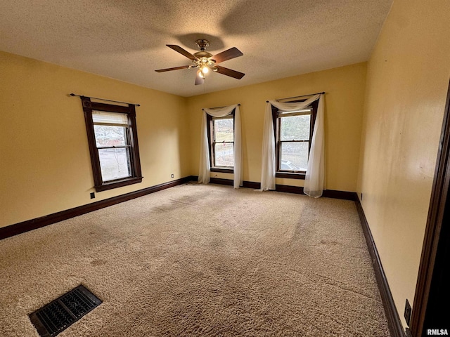 empty room with a textured ceiling, light colored carpet, a ceiling fan, baseboards, and visible vents