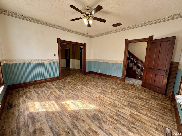 empty room featuring a textured ceiling, visible vents, wood finished floors, and wainscoting