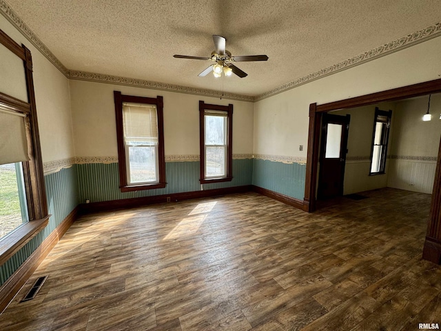 unfurnished room featuring a textured ceiling, dark wood-style flooring, wainscoting, and visible vents