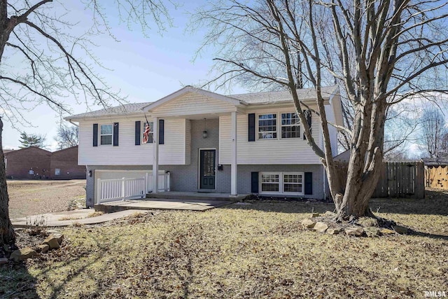 bi-level home with an attached garage, fence, and brick siding