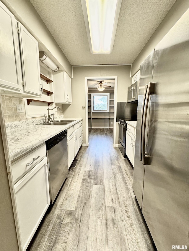 kitchen with stainless steel appliances, light wood finished floors, a sink, and white cabinets