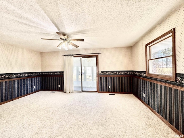 spare room with carpet floors, wallpapered walls, a textured ceiling, and a wainscoted wall