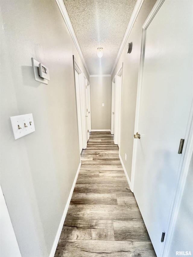 hallway featuring a textured ceiling, ornamental molding, light wood-type flooring, and baseboards