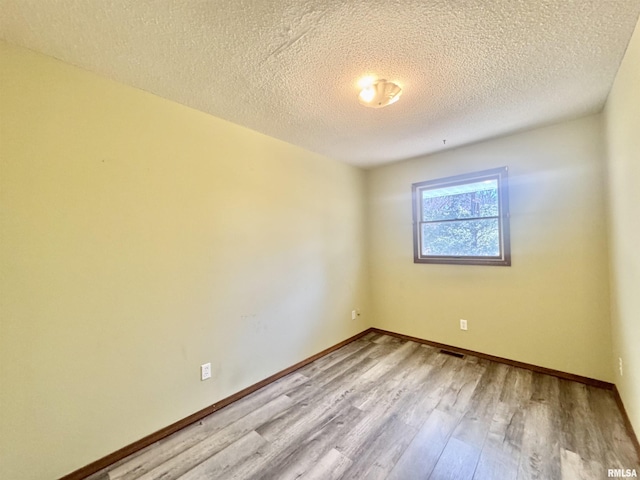 empty room with a textured ceiling, wood finished floors, and baseboards