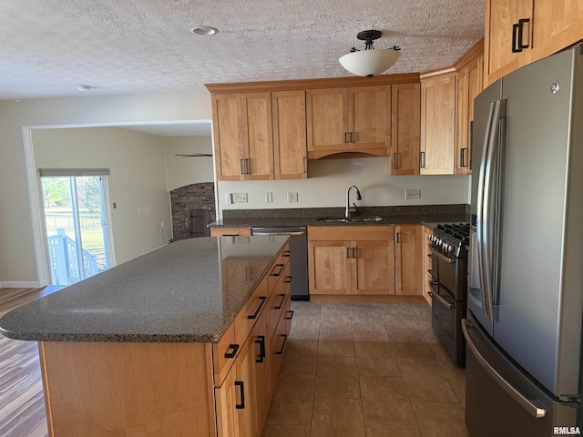 kitchen with a textured ceiling, a kitchen island, a sink, appliances with stainless steel finishes, and dark stone counters