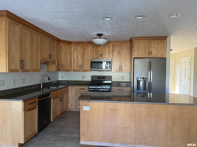 kitchen featuring a textured ceiling, a kitchen island, a sink, appliances with stainless steel finishes, and dark stone counters