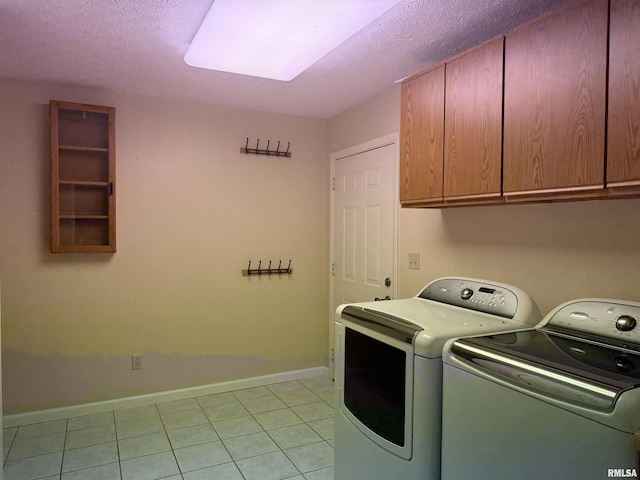 washroom featuring light tile patterned floors, a textured ceiling, baseboards, cabinet space, and washer and clothes dryer