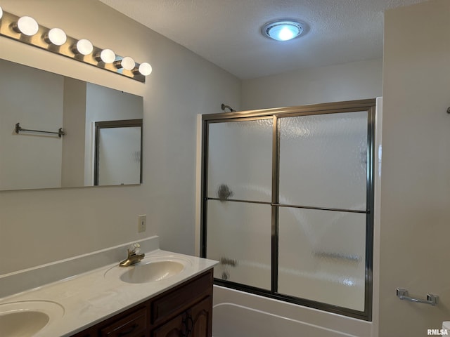 bathroom with double vanity, a textured ceiling, enclosed tub / shower combo, and a sink