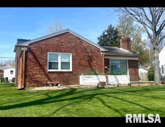 back of property with brick siding, a chimney, and a lawn