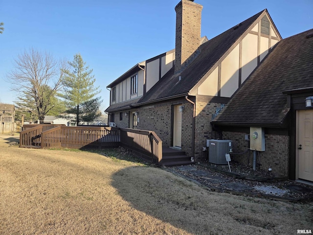 back of property featuring a chimney, stucco siding, a lawn, central AC unit, and a deck