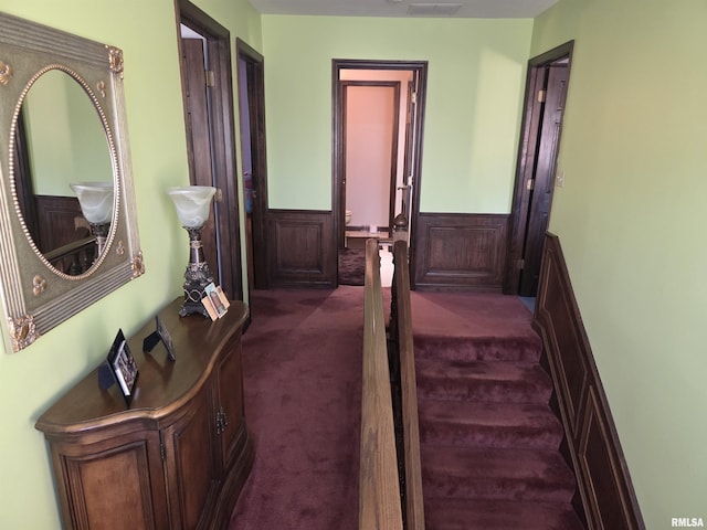 corridor with a wainscoted wall and dark colored carpet