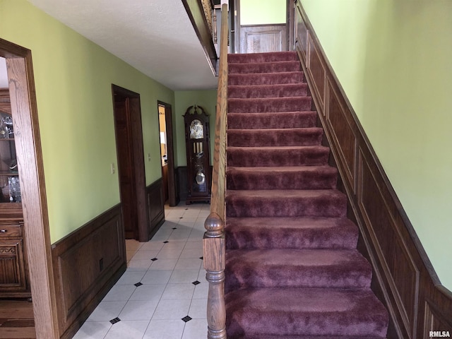 staircase featuring tile patterned flooring and a wainscoted wall