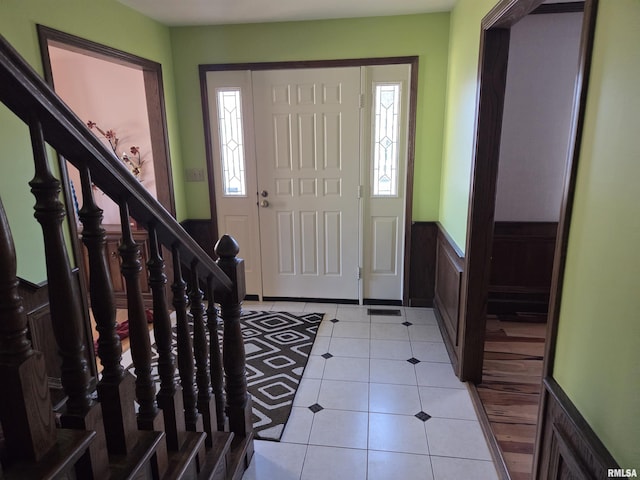 foyer featuring light tile patterned floors, stairway, and wainscoting