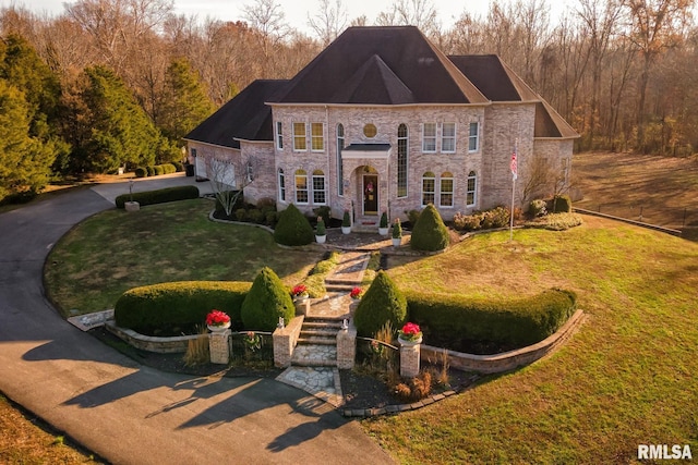 georgian-style home featuring stone siding, driveway, a front lawn, and fence