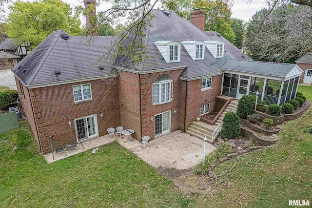 back of house with brick siding, a yard, a chimney, a sunroom, and a patio area