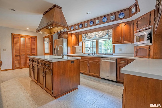 kitchen with light countertops, appliances with stainless steel finishes, brown cabinetry, a kitchen island with sink, and a sink