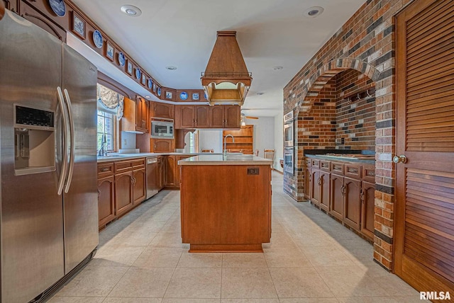 kitchen with light countertops, appliances with stainless steel finishes, brown cabinetry, a sink, and brick wall