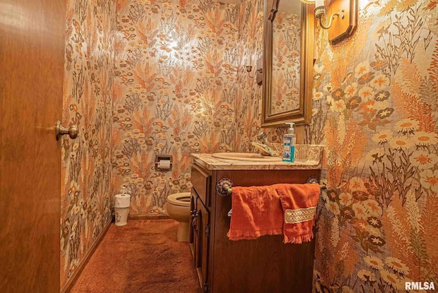 half bathroom featuring toilet, wallpapered walls, and vanity