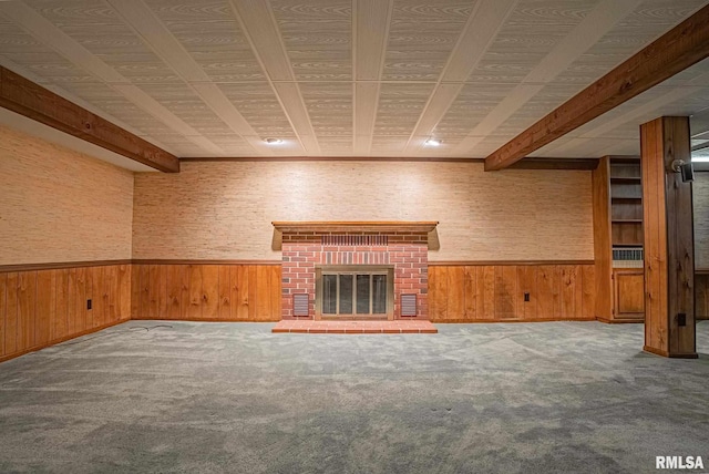 unfurnished living room featuring a wainscoted wall, wooden walls, a brick fireplace, and beam ceiling