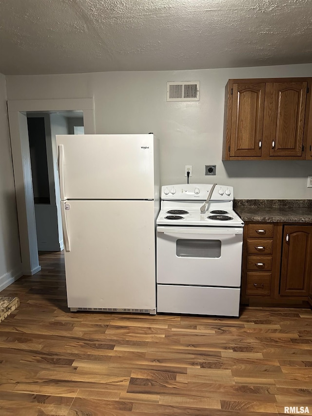 kitchen with dark countertops, visible vents, white appliances, and dark wood-style floors