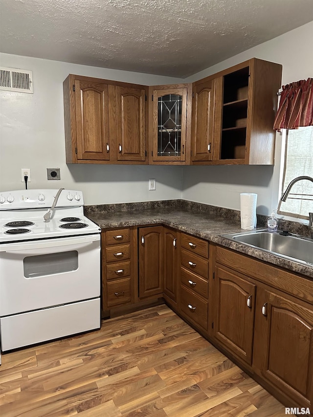 kitchen featuring visible vents, white range with electric cooktop, a sink, dark countertops, and light wood finished floors