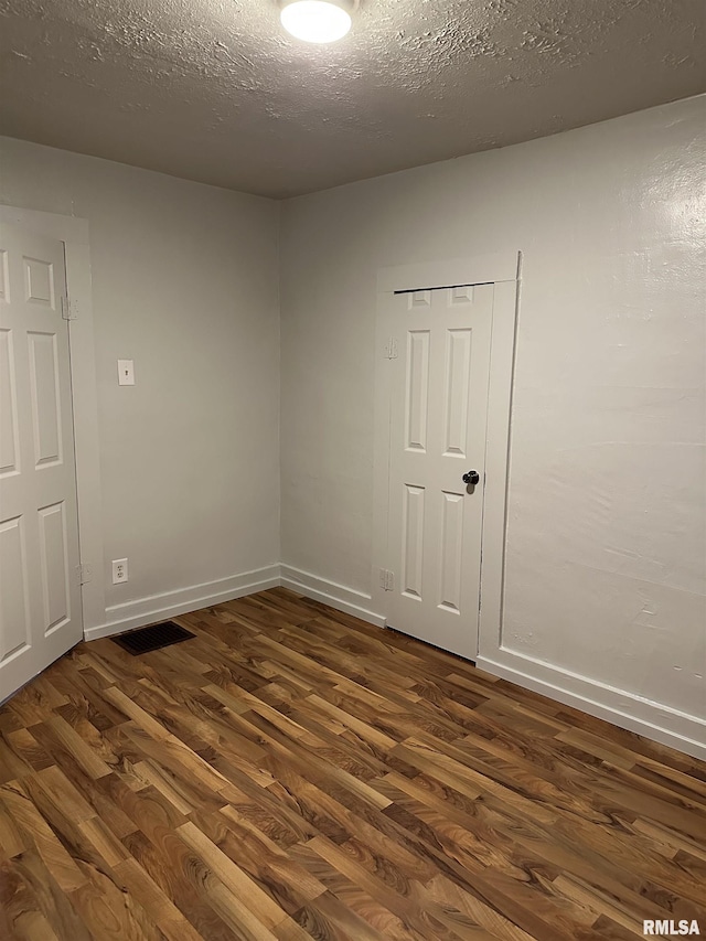 unfurnished room featuring visible vents, baseboards, a textured ceiling, and dark wood-style floors