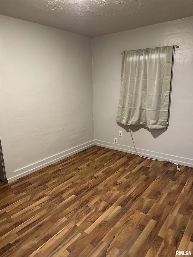 spare room with baseboards, dark wood-type flooring, and a textured ceiling