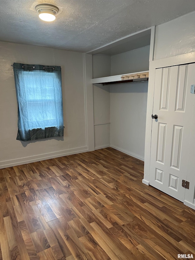 unfurnished bedroom with baseboards, a textured ceiling, and dark wood-style flooring