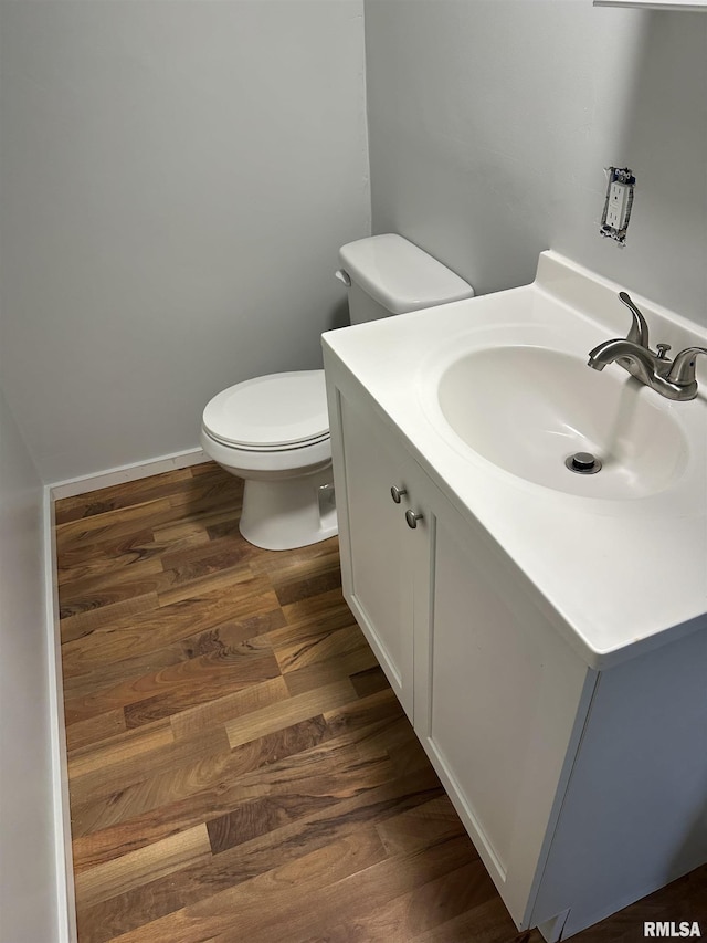 half bathroom featuring toilet, vanity, baseboards, and wood finished floors