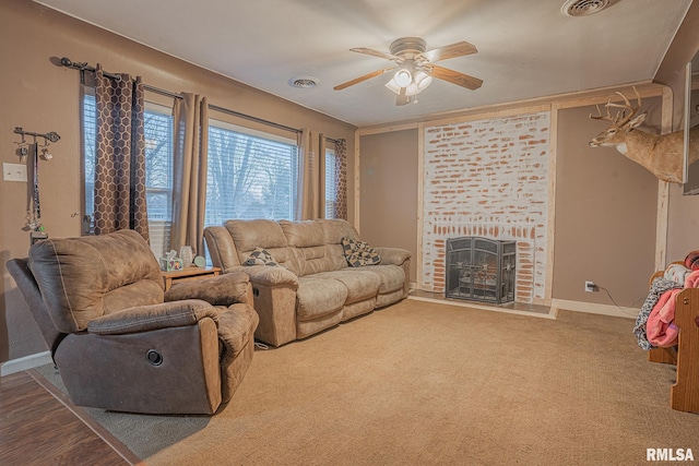 living room with carpet flooring, a ceiling fan, visible vents, baseboards, and a brick fireplace