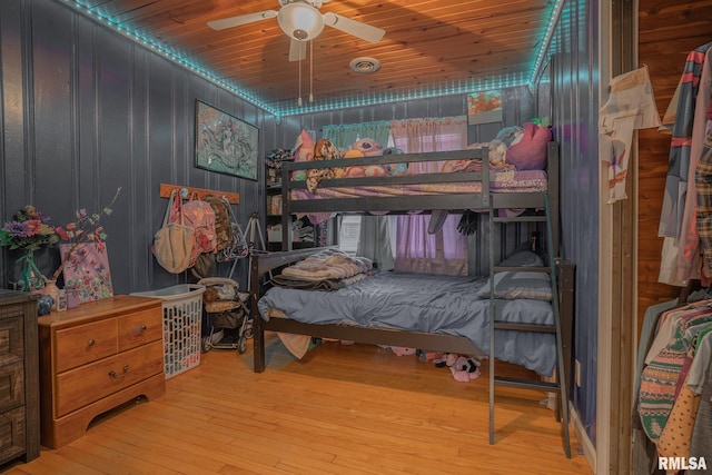 bedroom featuring a ceiling fan, wooden ceiling, wood walls, and hardwood / wood-style floors