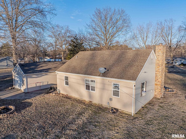 view of home's exterior featuring a shingled roof, an outbuilding, and a chimney