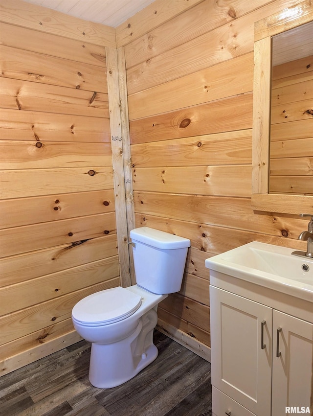 half bathroom with wood finished floors, wood walls, vanity, and toilet