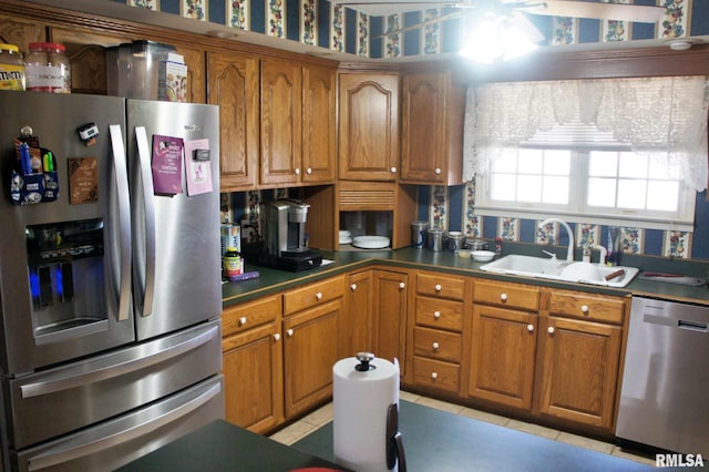 kitchen with dark countertops, brown cabinets, stainless steel appliances, a sink, and light tile patterned flooring