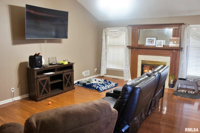 living area with baseboards, visible vents, a premium fireplace, wood finished floors, and vaulted ceiling