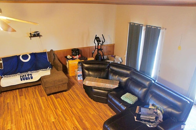 living room featuring ceiling fan, wood walls, wainscoting, and wood finished floors