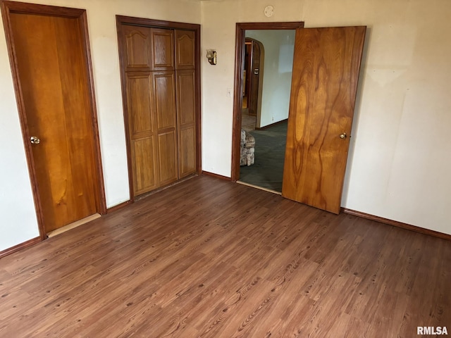 unfurnished bedroom featuring two closets, baseboards, and wood finished floors