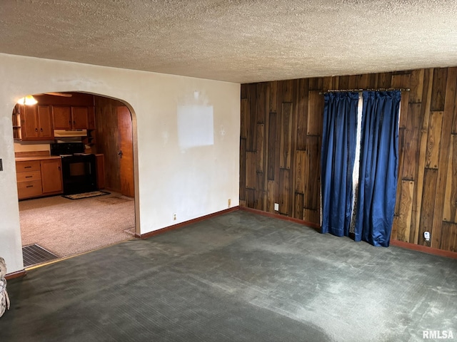 carpeted spare room featuring arched walkways, wood walls, a textured ceiling, and visible vents