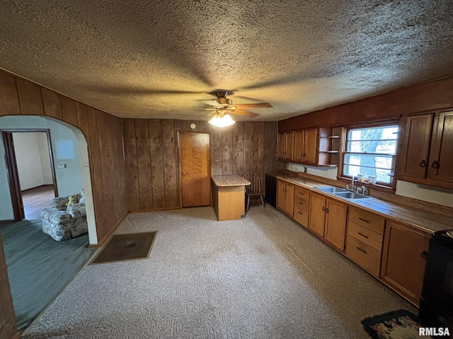 kitchen featuring arched walkways, light colored carpet, a sink, wooden walls, and range