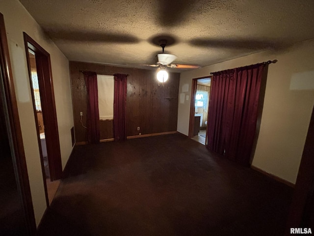 spare room with a textured ceiling, dark colored carpet, a ceiling fan, and wooden walls