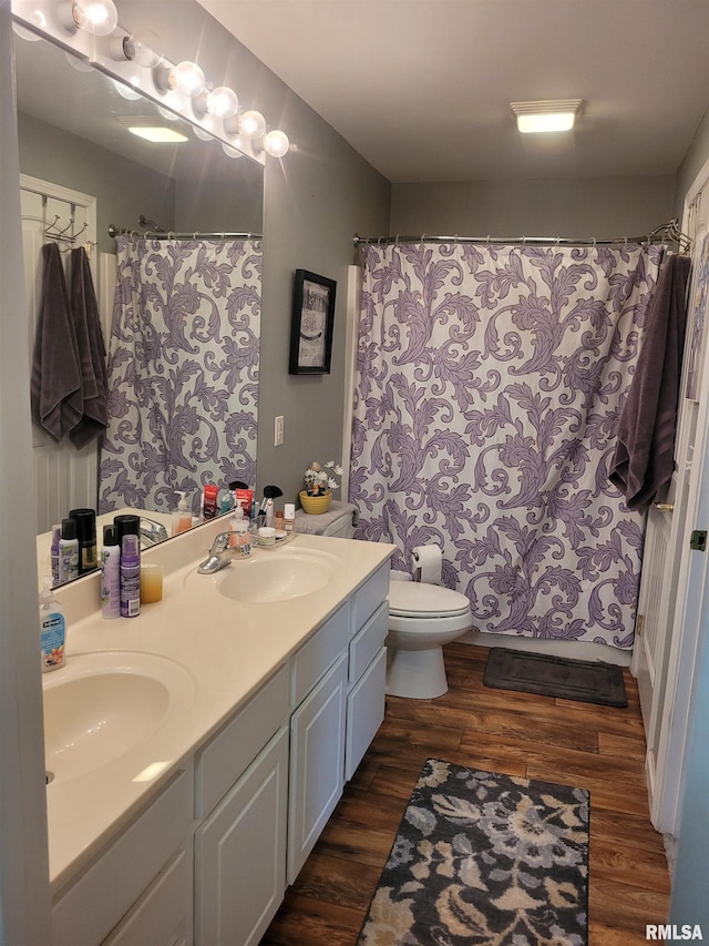 full bathroom with double vanity, a sink, toilet, and wood finished floors