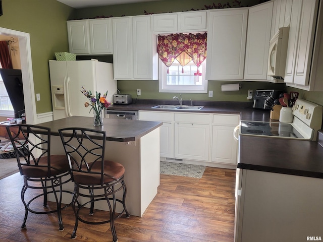 kitchen featuring dark countertops, white cabinets, a sink, white appliances, and a kitchen bar