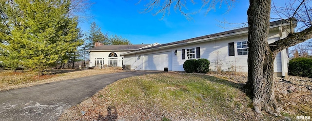 ranch-style house featuring aphalt driveway, a chimney, and an attached garage